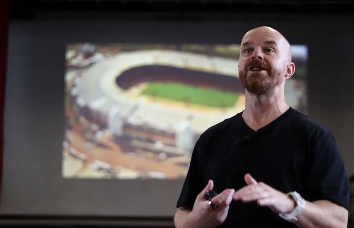 Luke Staton on stage, telling the story in front of a picture of the old Wembley Stadium.